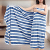 A woman is holding a blue and white striped microfiber bath towel draped over her shoulder.