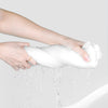 A hand is squeezing a white disposable compressed washcloth, with water dripping from it.