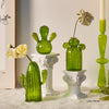 Collection de vases en cactus verts et vibrants sur des socles blancs contre un fond clair.