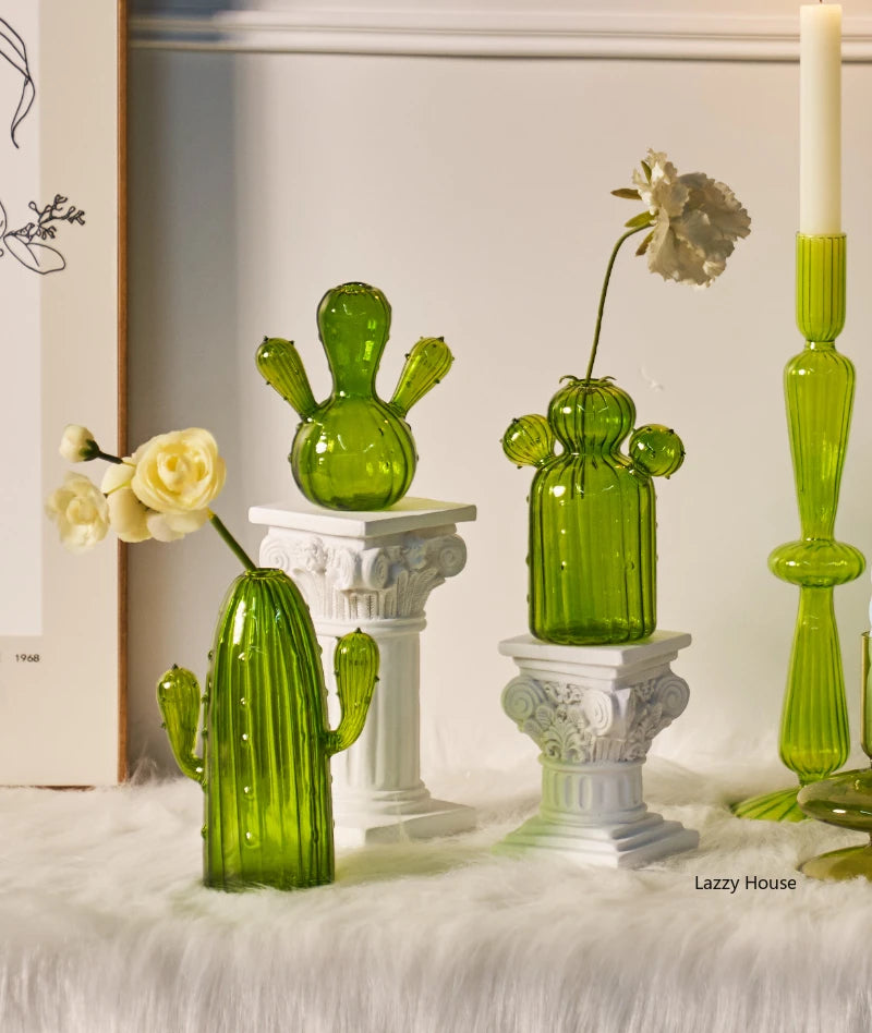Collection de vases en cactus verts et vibrants sur des socles blancs contre un fond clair.