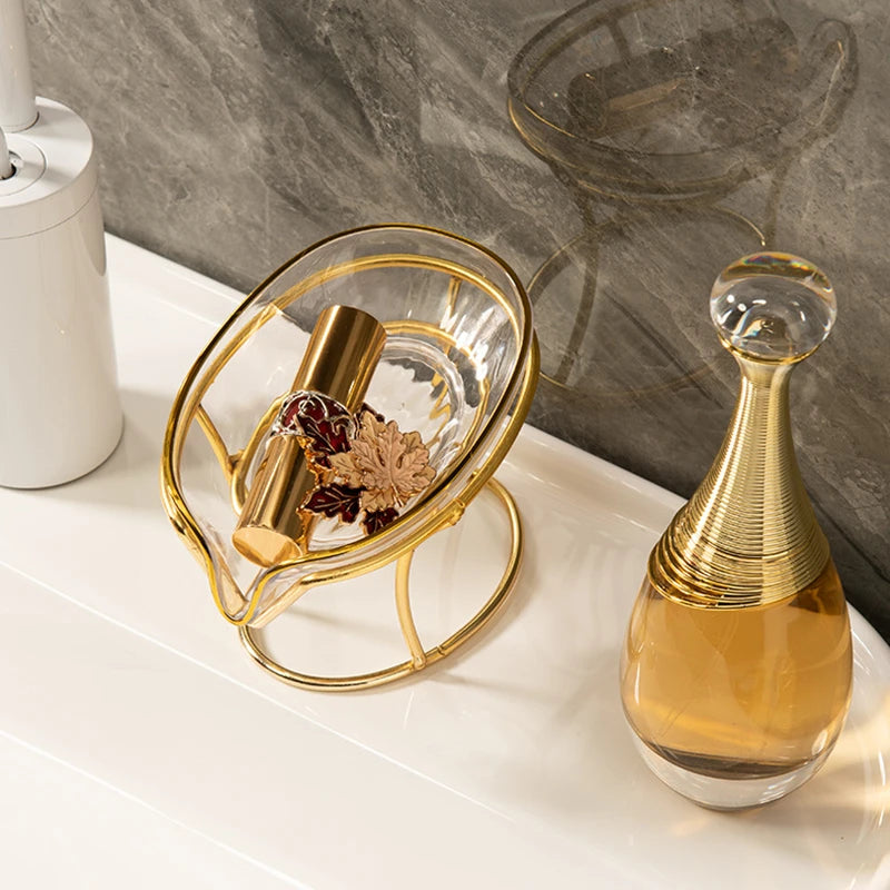 A gold leaf soap dish with a glass bowl and a golden soap dispenser sitting on a white countertop.