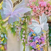 A decorative display featuring large, translucent butterfly shapes made of fabric and surrounded by colorful floral greenery.