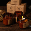A brown soy wax candle in a glass jar sits next to two boxes labeled Delicate Aroma.
