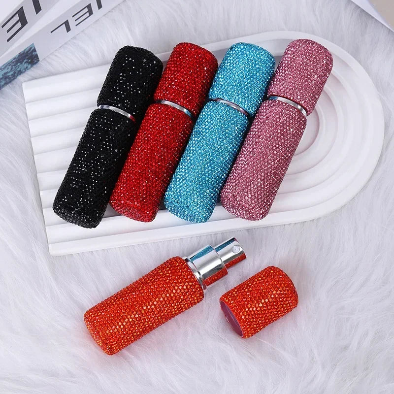 A row of seven glass perfume spray bottles in various colors including black, red, blue, and pink, displayed on a white surfa