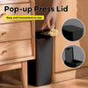 A hand is pressing a pop-up press lid onto a black trash can in a wooden cabinet setting.