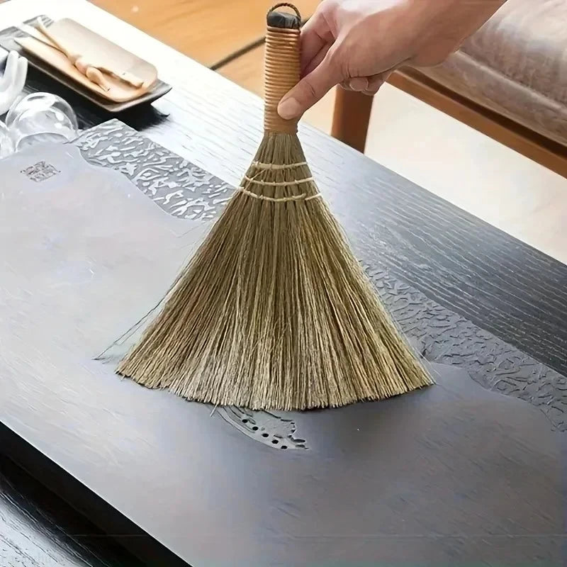 Eine Hand hält eine natürliche Grasmäher mit geflochtenem Griff über einer grauen Holzoberfläche.