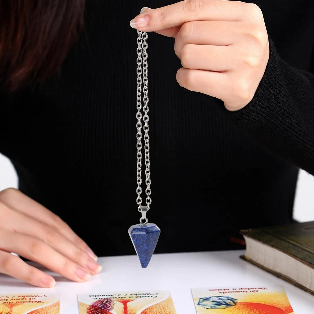 A hand holds a silver crystal necklace with a blue pendant against a black background.