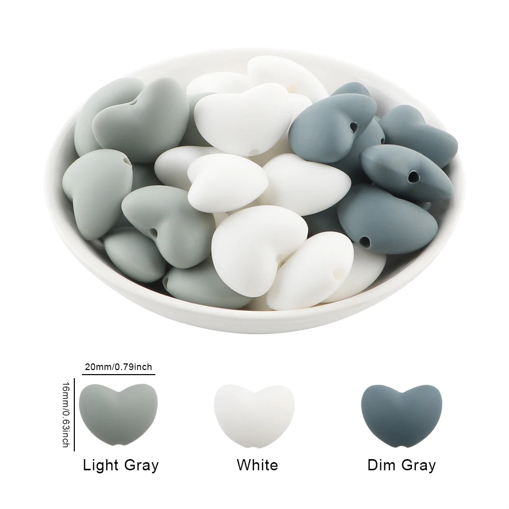 A bowl filled with ten silicone heart-shaped charm beads in light gray, white, and dim gray colors.