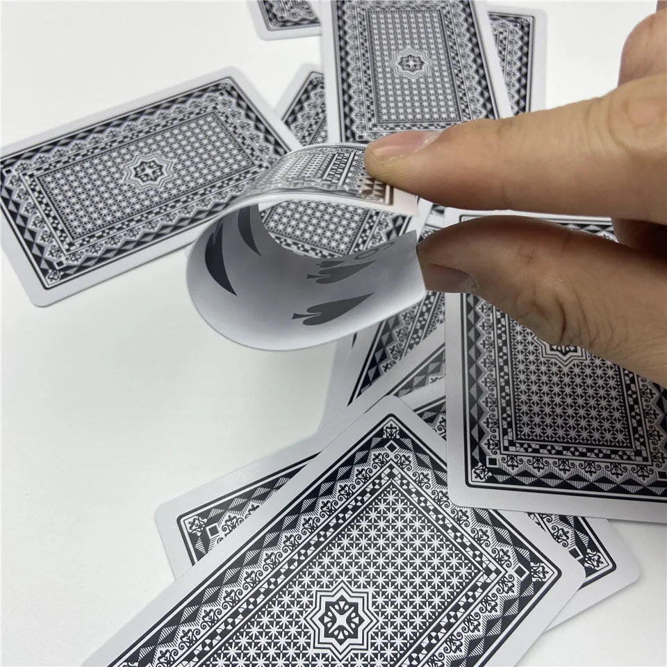 A hand is holding and examining a stack of black and white patterned poker playing cards.