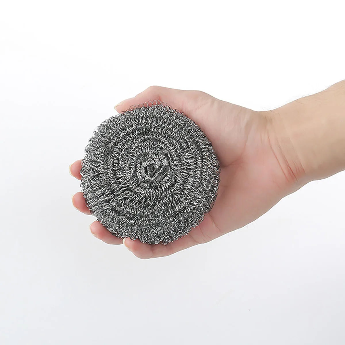 A hand holds a circular pad of gray stainless steel scrubber material.