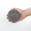 A hand holds a circular pad of gray stainless steel scrubber material.