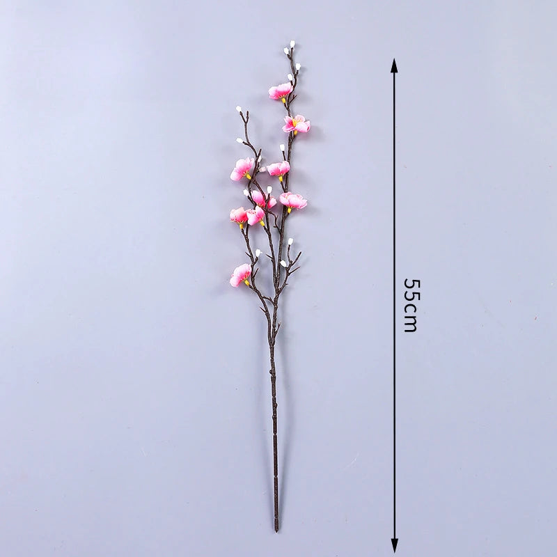 Eine schlanke Zweig aus künstlichen rosa Pflaumenblüten mit kleinen weißen Akzenten, präsentiert vor grauem Hintergrund und e