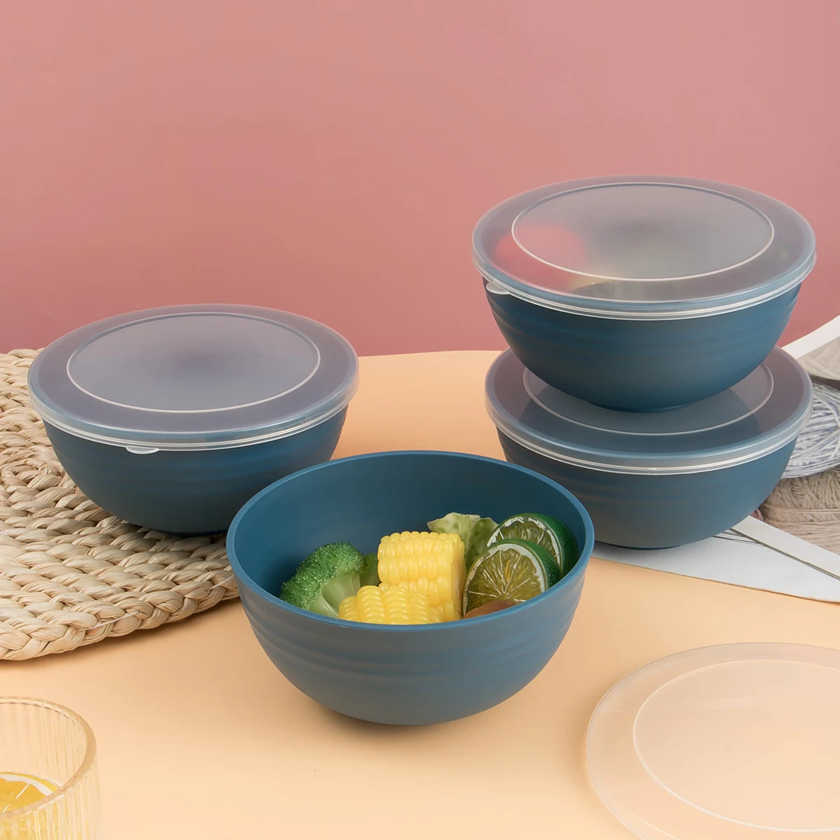 A stack of dark blue reusable food storage bowls with clear lids filled with green and yellow vegetables on a light orange su