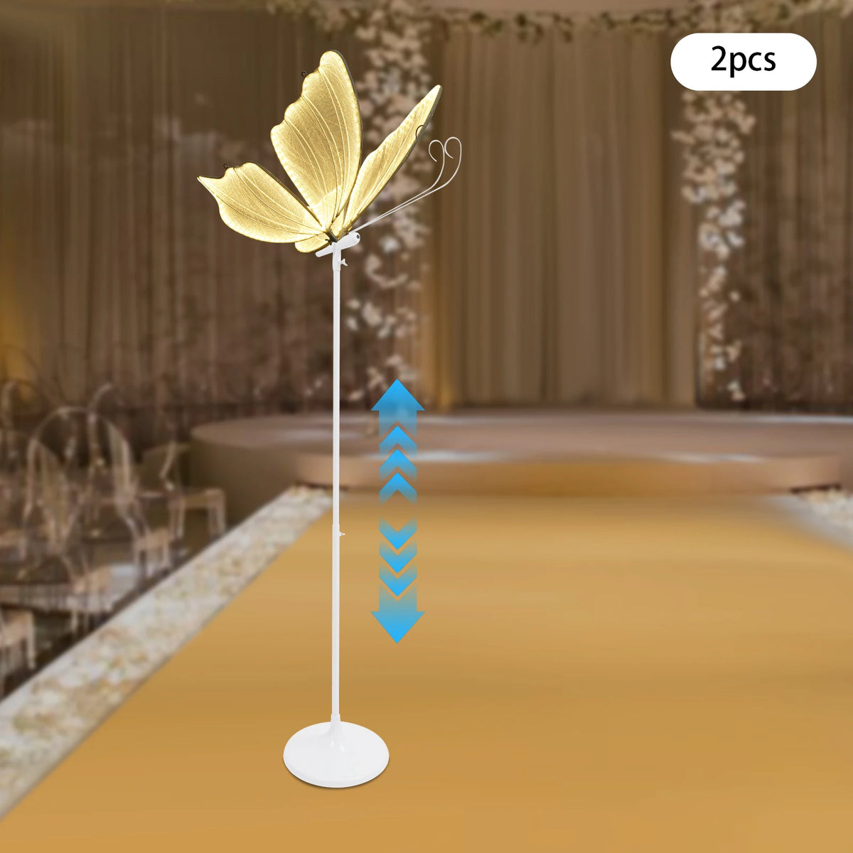 Ein Set aus zwei goldenen Schmetterlings-LED-Bodenlampen auf einem weißen Ständer vor unscharfem Hintergrund.