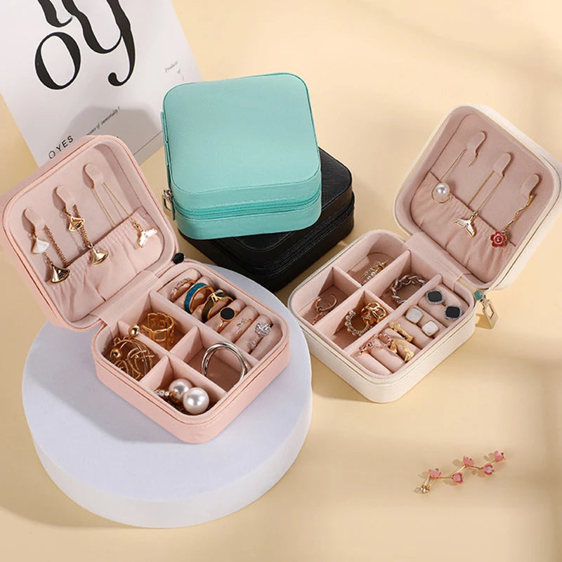 A pink portable PU leather jewelry storage box with a teal fabric pouch and various gold and silver jewelry items.
