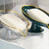 An oval white soap dish with a gold rim and drainage holes is shown on a white surface.