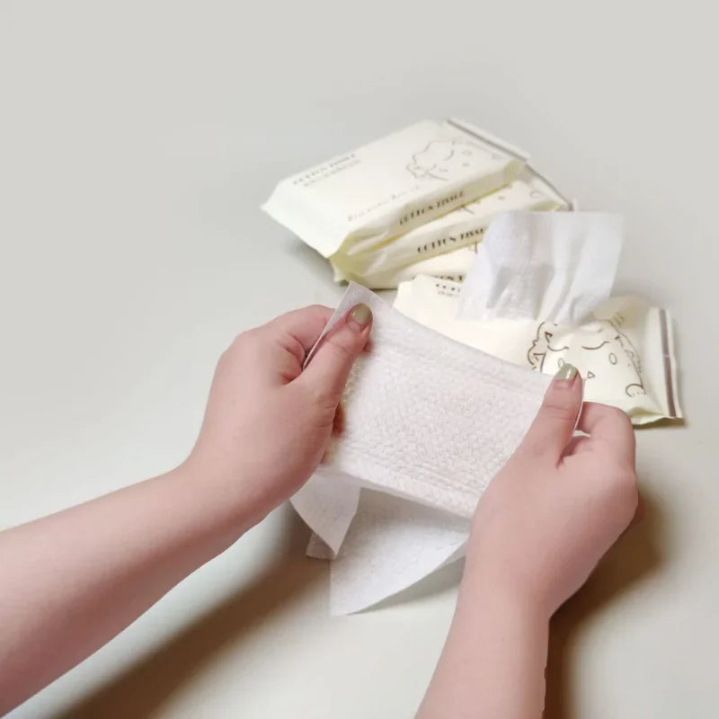 Hands are holding a stack of disposable facial cleansing wipes and a sheet of white wipe.