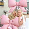 A woman is surrounded by large pink balloon decorations shaped like bows and flowers.