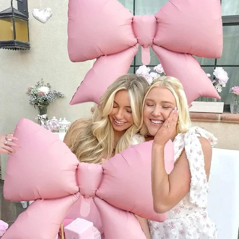 A woman is surrounded by large pink balloon decorations shaped like bows and flowers.