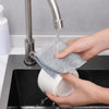 A hand is using a metal faucet to pour water onto a mesh cleaning cloth placed in a black sink.