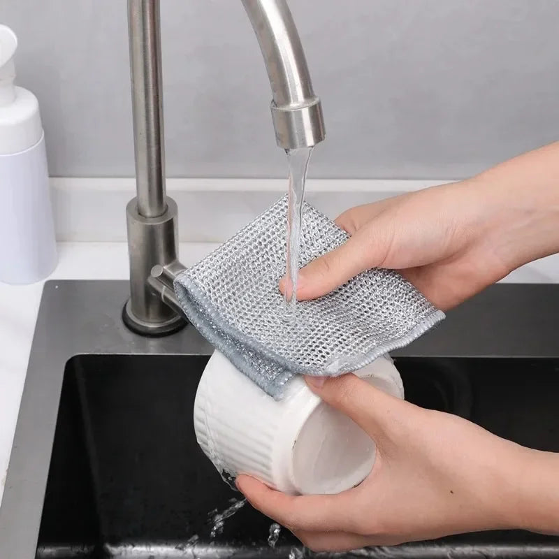 A hand is using a metal faucet to pour water onto a mesh cleaning cloth placed in a black sink.