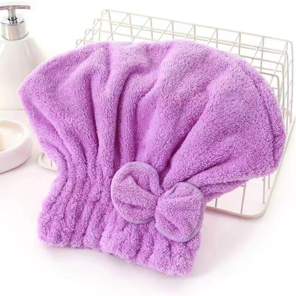 A purple microfiber hair drying cap and towel with a bow is displayed in a wire basket.