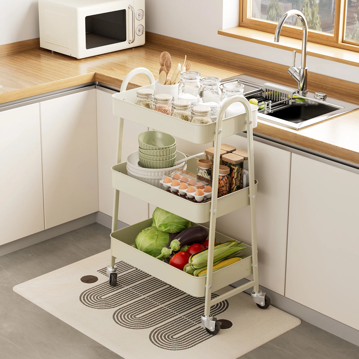 A white 3-tier metal rolling storage cart filled with various kitchen items like jars and produce on a countertop.