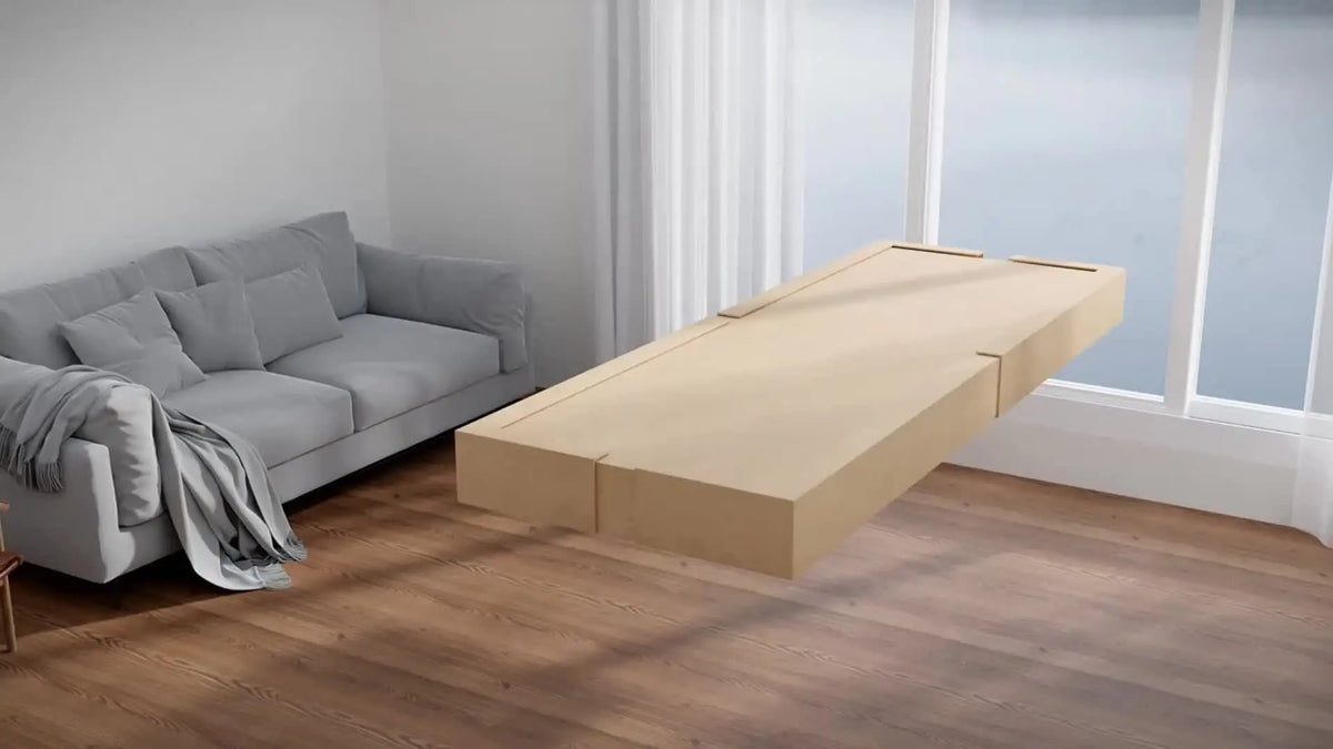 A light wood storage box is placed on a wooden floor next to a gray sofa and a large window.