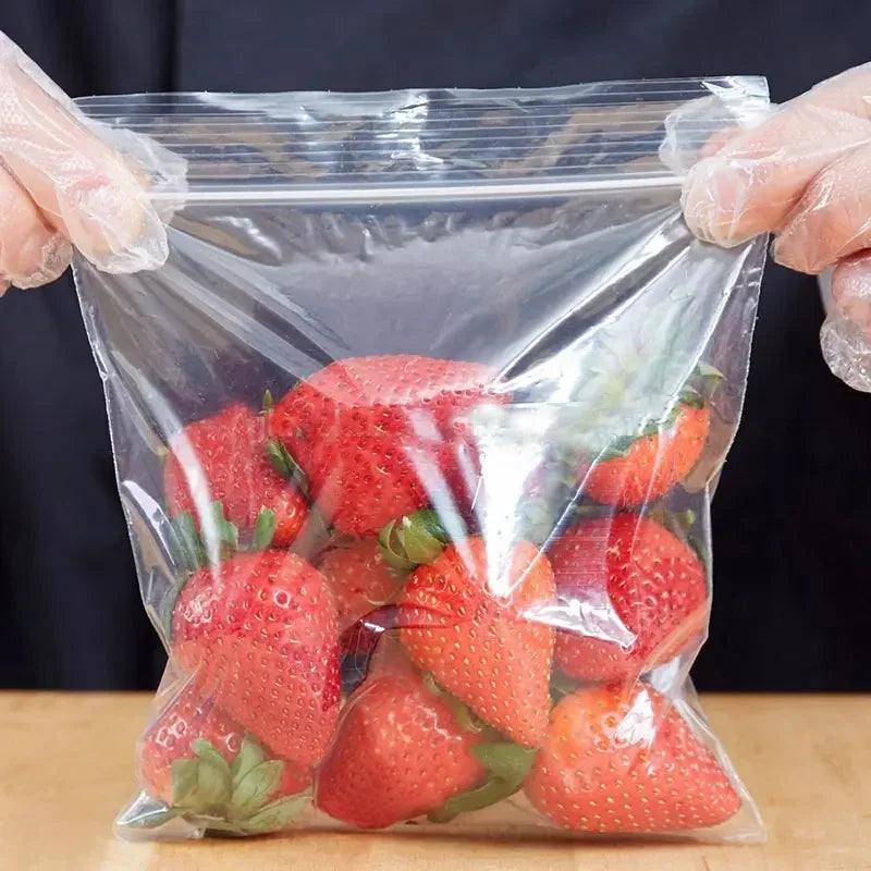 Manos colocando fresas frescas en una bolsa reutilizable con cierre ziplock transparente.
