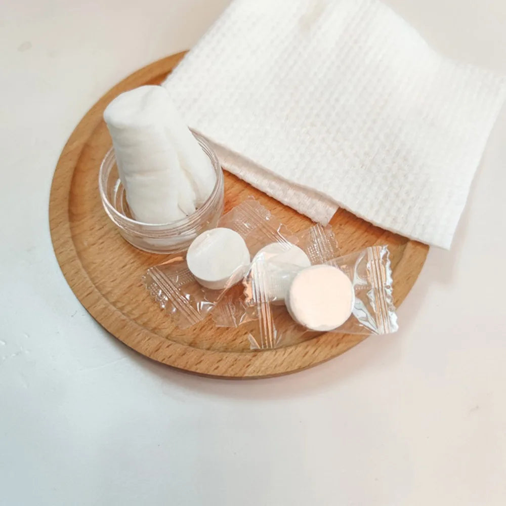 A set of disposable compressed travel towels in a glass jar and clear plastic packaging on a wooden plate.