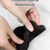 A hand is using a black thickened material sponge to remove water droplets from a white surface.