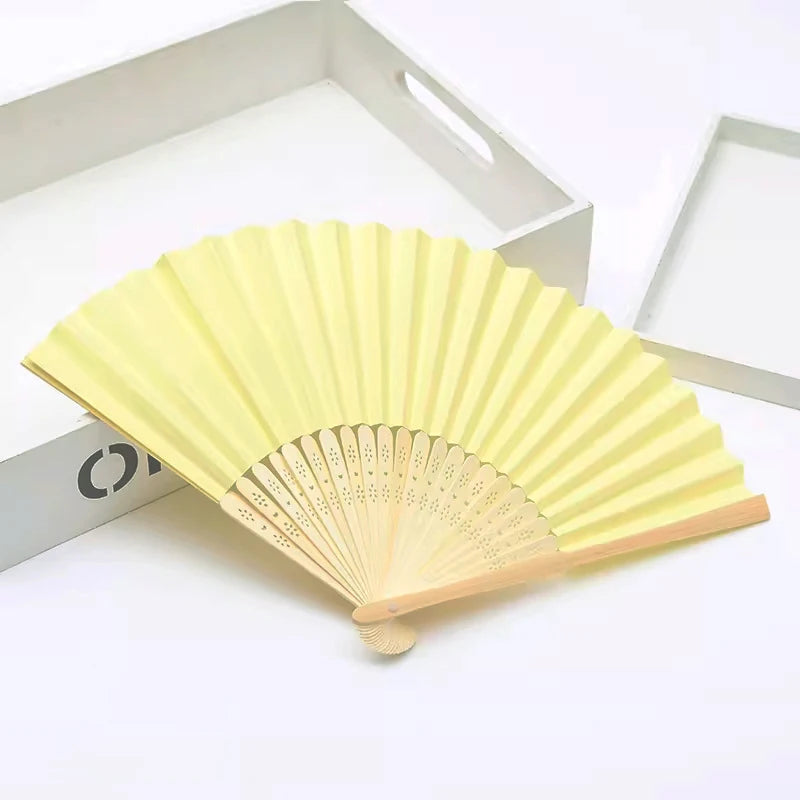 Un éventail pliable jaune en bambou et papier, ouvert sur fond blanc.
