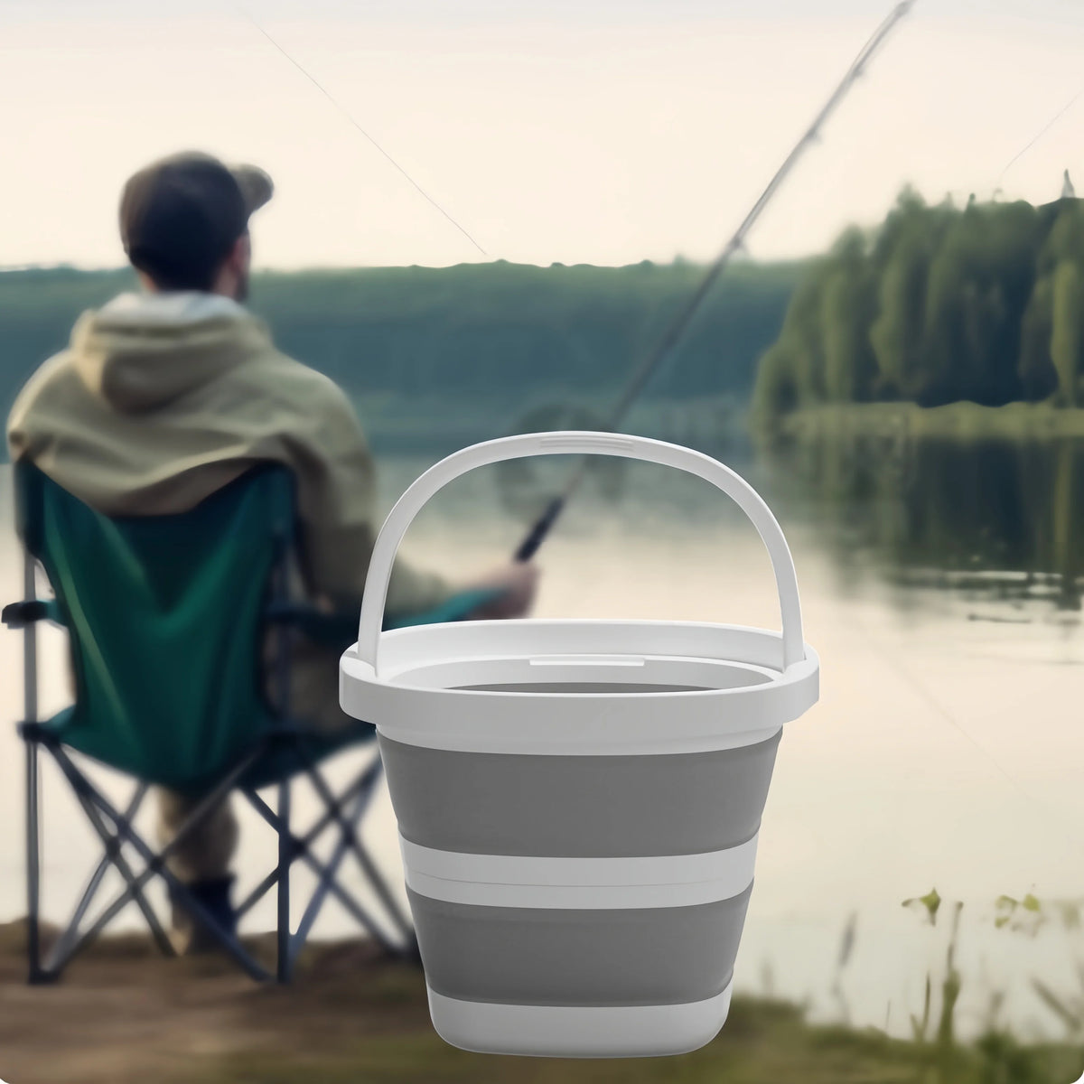 A person is sitting by a body of water with a white collapsible bucket in front of them.