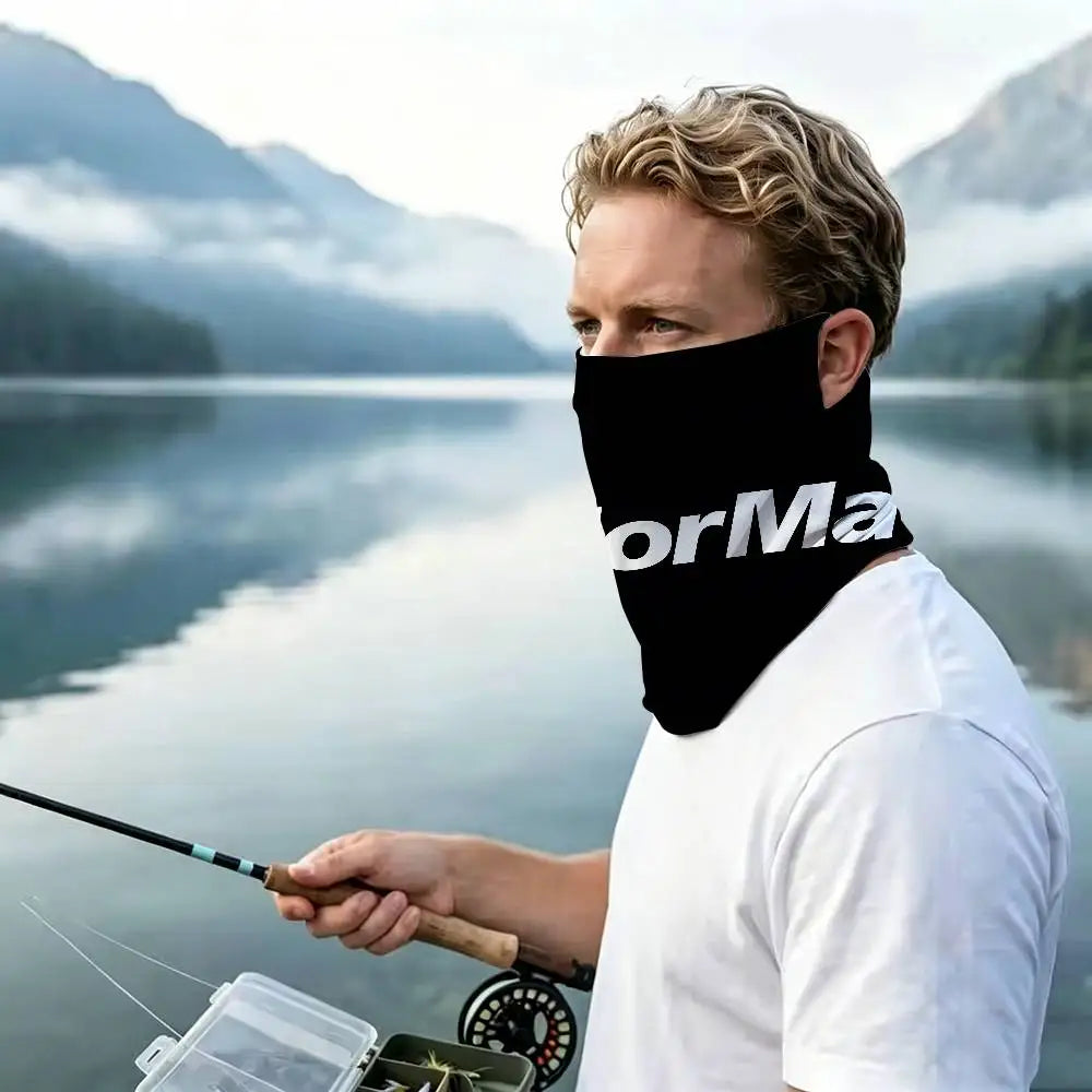A man wearing a black windproof neck gaiter is fishing on a body of water with mountains in the background.