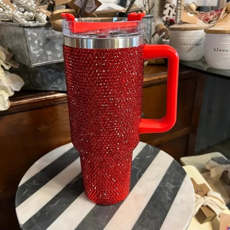 Termo aislado de acero inoxidable con strass rojos y tapa transparente, mostrado sobre una superficie de patrón blanco y negr