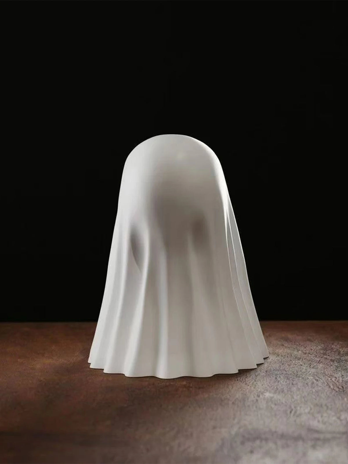 A smooth, white ghost statue decoration is shown from the back against a dark background.