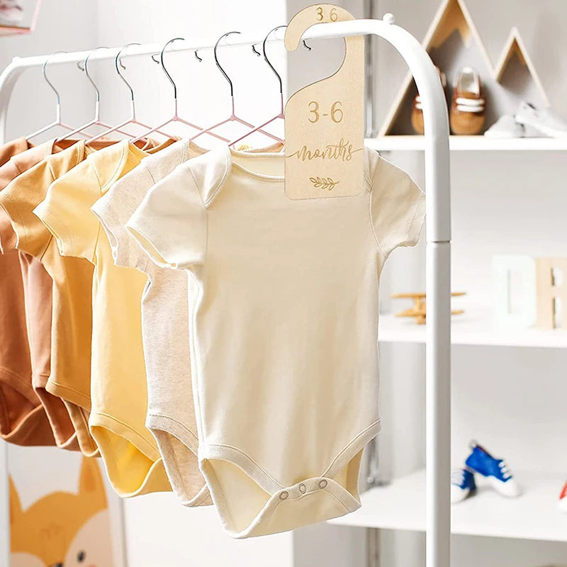A wooden baby closet divider set displaying several cream and yellow short-sleeved baby bodysuits on a white hanger.
