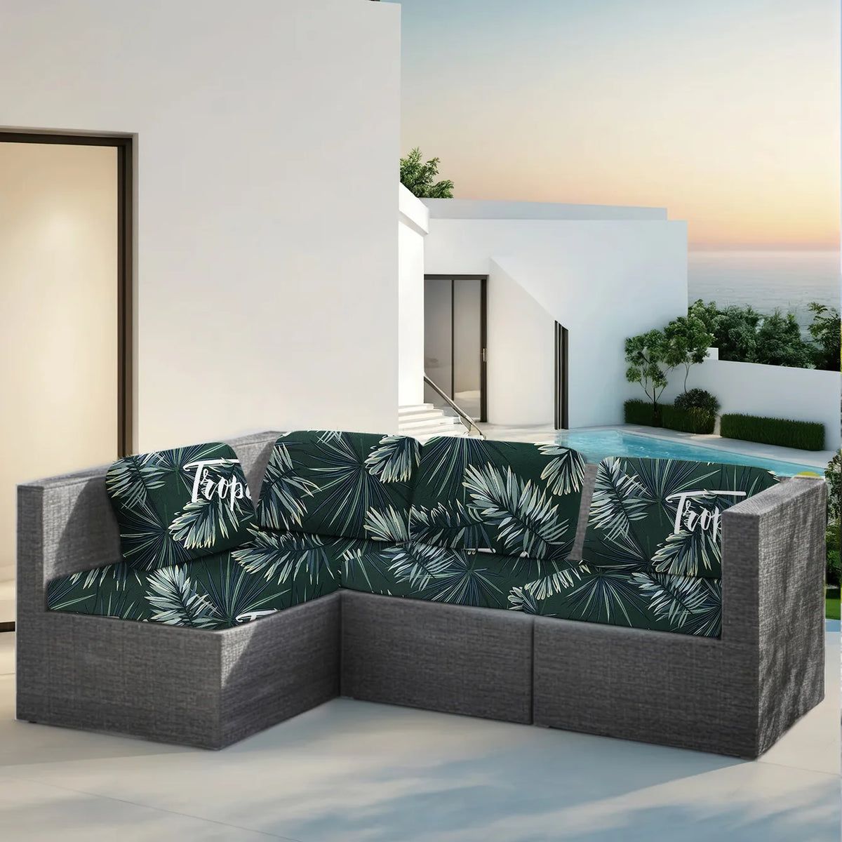 Una funda para sofá exterior verde oscuro con estampado de hoja tropical, colocada en un patio cerca de una piscina y arquite