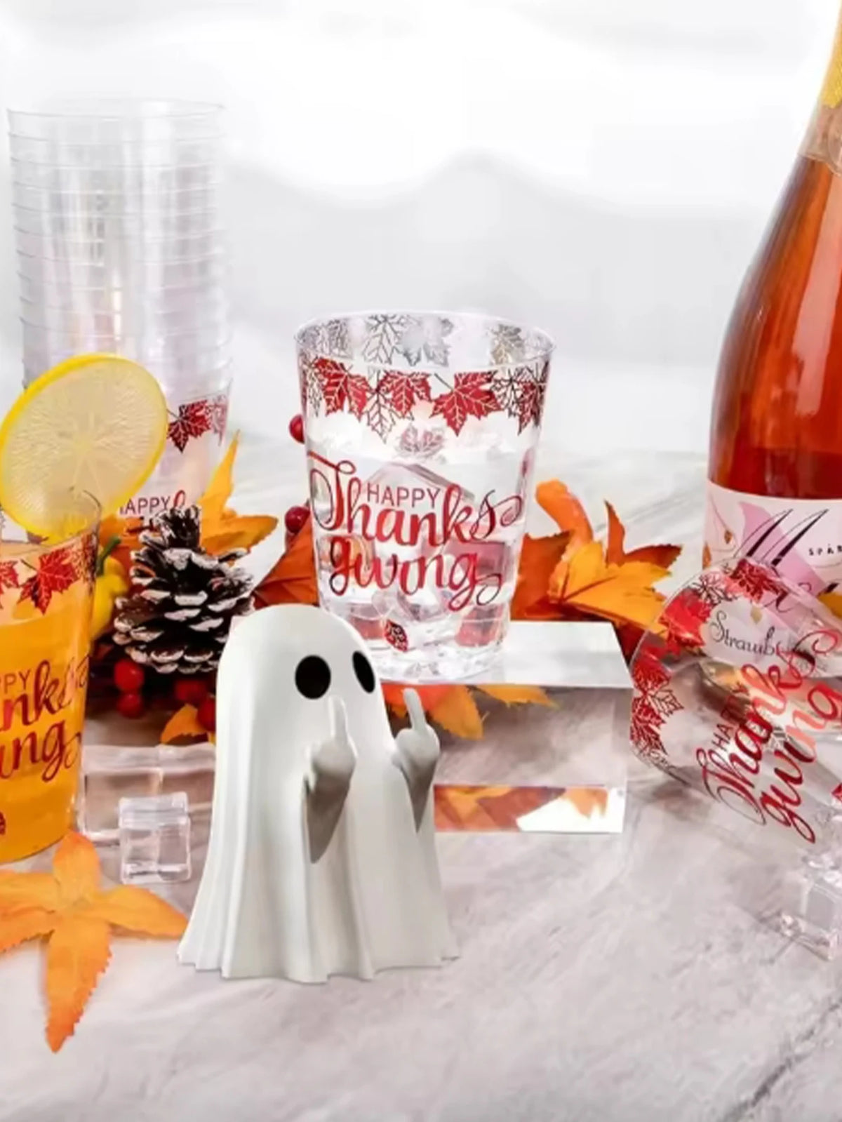 A white ghost statue decoration is displayed with citrus slices, autumn leaves, and a glass featuring holiday-themed text.