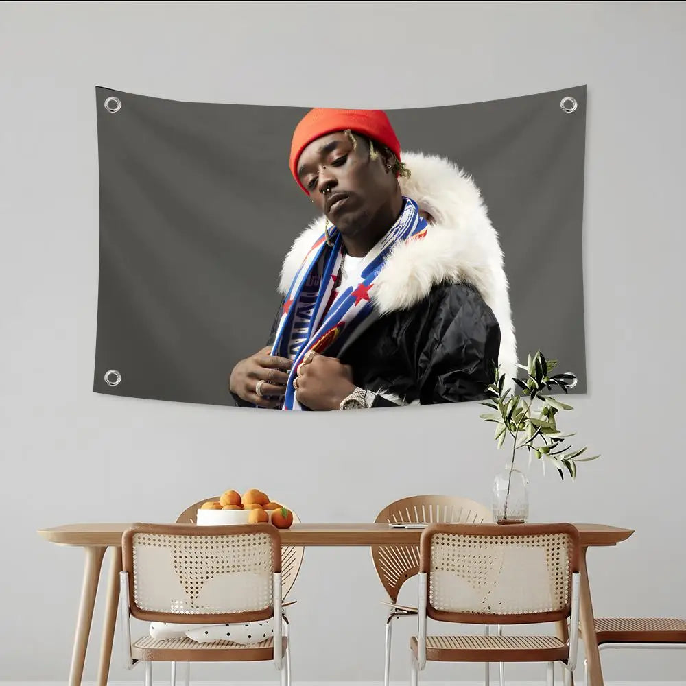 Ein Mann mit orangefarbem Hut und Pelzkragen vor schwarzem Flaggenhintergrund.