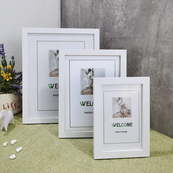 Three white photo frames of varying sizes displayed on a light green surface against a gray textured wall.