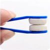 A hand holds a blue cleaning brush with two white microfiber pads for cleaning eyeglasses.