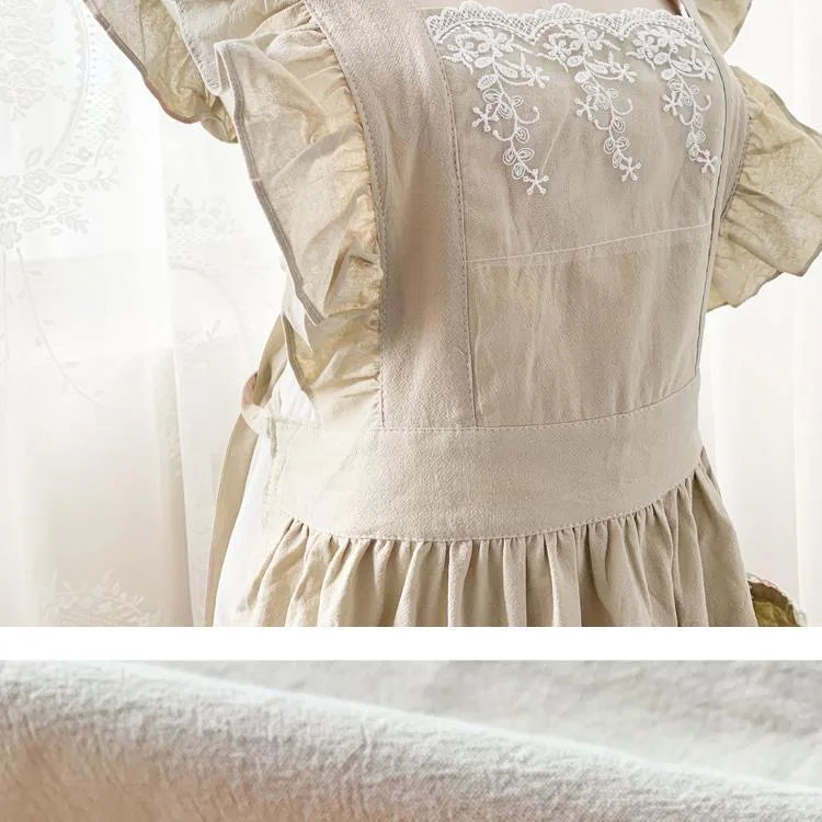 A light beige cotton linen kitchen apron featuring delicate white lace detailing and ruffled fabric.