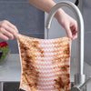 A hand is using a faucet to fill a thickened coral velvet cleaning cloth with water.