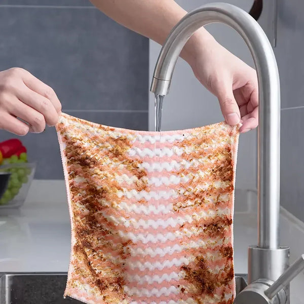 A hand is using a faucet to fill a thickened coral velvet cleaning cloth with water.
