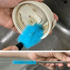 A hand holds a bright blue bottle brush and a wire brush set in a stainless steel sink.