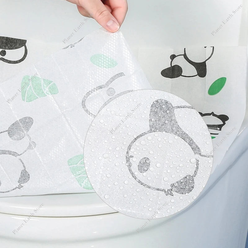 A hand is placing a disposable printing seat cover onto a toilet seat.
