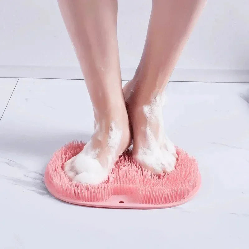 Un par de pies descalzos descansando sobre una estera de ducha de masaje de silicona rosa con espuma blanca.