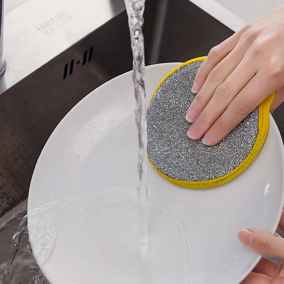A hand is rinsing a reusable double-sided dishwashing sponge set under running water in a white bowl.