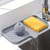 A yellow silicone mat is placed in a kitchen sink, featuring a sponge ball and a block of cheese.
